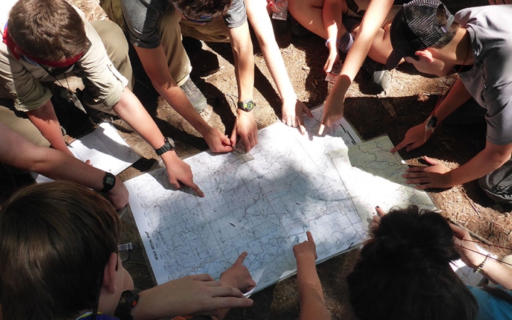 A group of students point at a map laying on the ground.